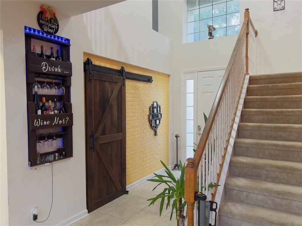 An entryway features a carpeted staircase, a wooden barn door, and a wall-mounted wine rack — 992 NODDING SHADE DRIVE, BROOKSVILLE, FL