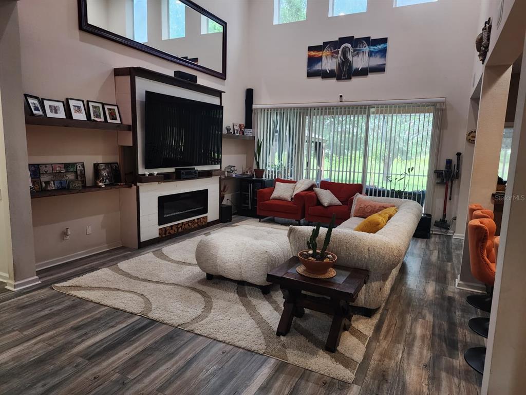 A living room features a fireplace, a large television, red armchairs, and a white sofa — 992 NODDING SHADE DRIVE, BROOKSVILLE, FL