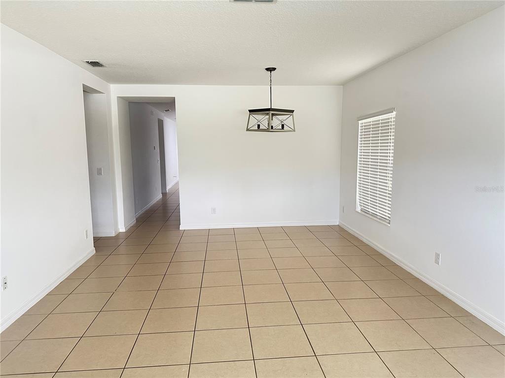 An empty dining room features beige tile flooring, white walls, and a modern rectangular chandelier — 477 KESTREL DRIVE, GROVELAND, FL