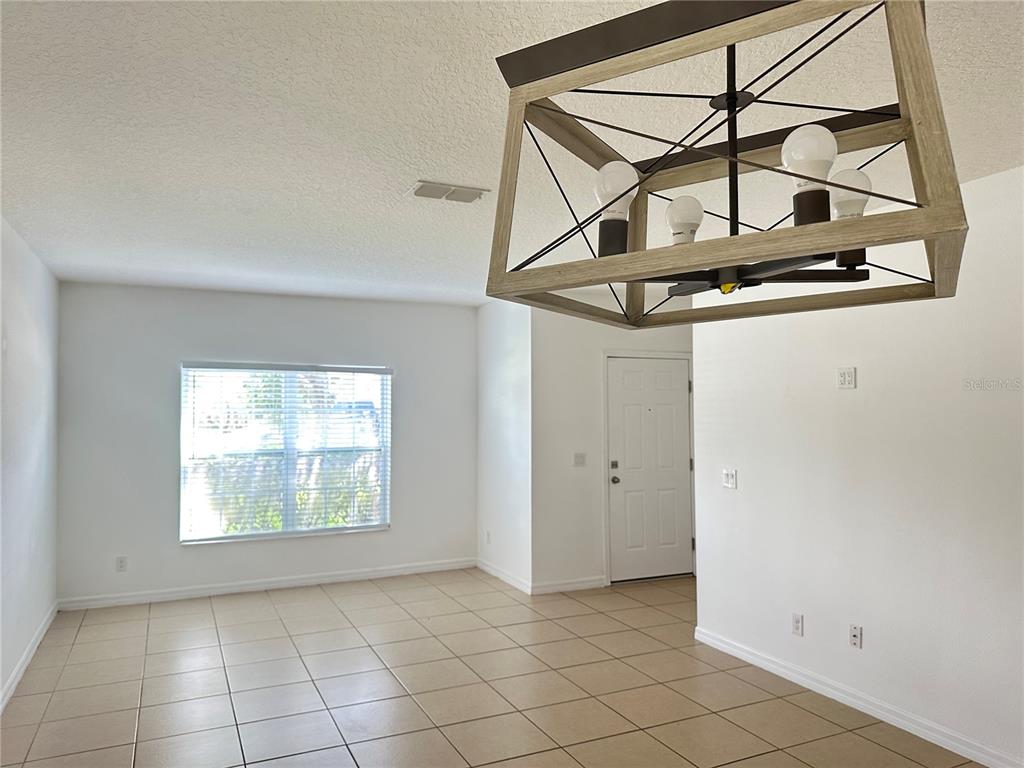 A dining area features beige tile flooring, a large window, and a wooden chandelier — 477 KESTREL DRIVE, GROVELAND, FL