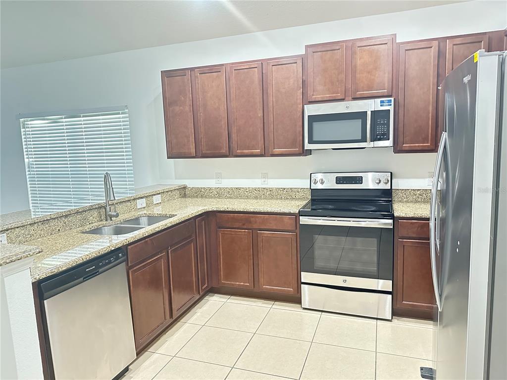 A kitchen features dark wood cabinets, granite countertops, stainless steel appliances, and tile flooring — 477 KESTREL DRIVE, GROVELAND, FL