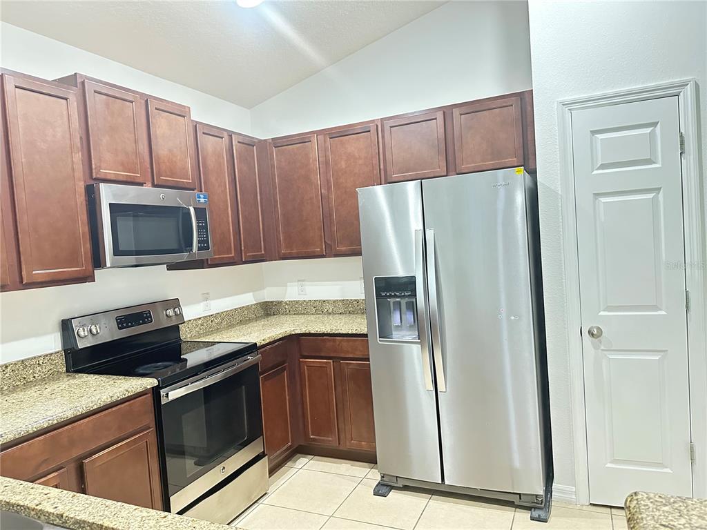 A kitchen features dark wood cabinets, granite countertops, stainless steel appliances, and tile flooring — 477 KESTREL DRIVE, GROVELAND, FL