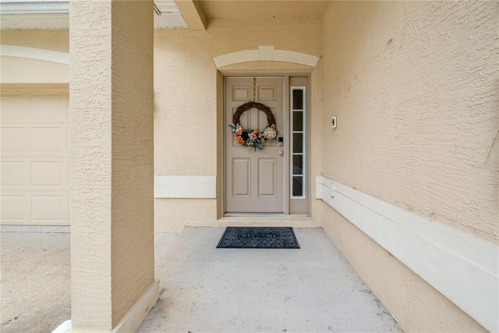 A beige stucco house exterior features a front door with a wreath and a sidelight — 14369 NW 159TH PLACE, ALACHUA, FL