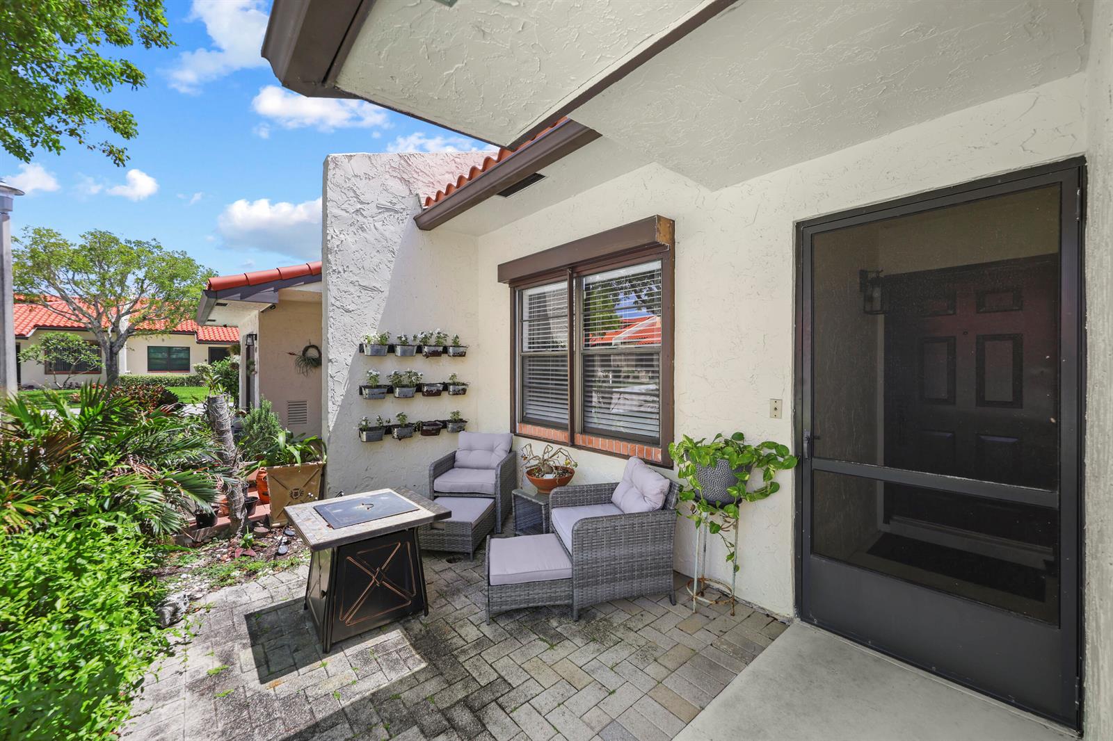 A paved patio features a fire pit, two wicker chairs with ottomans, and wall-mounted planters — 39 Bethesda Park Circle # L39, Boynton Beach FL 33435, BOYNTON BEACH, FL