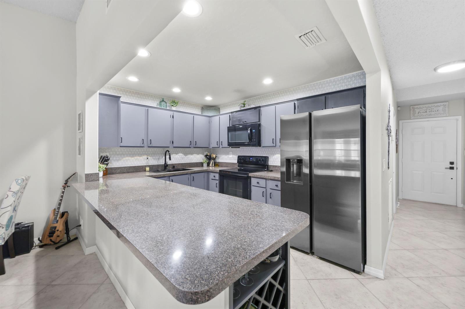 A kitchen features gray cabinets, granite countertops, stainless steel appliances, and a breakfast bar — 39 Bethesda Park Circle # L39, Boynton Beach FL 33435, BOYNTON BEACH, FL