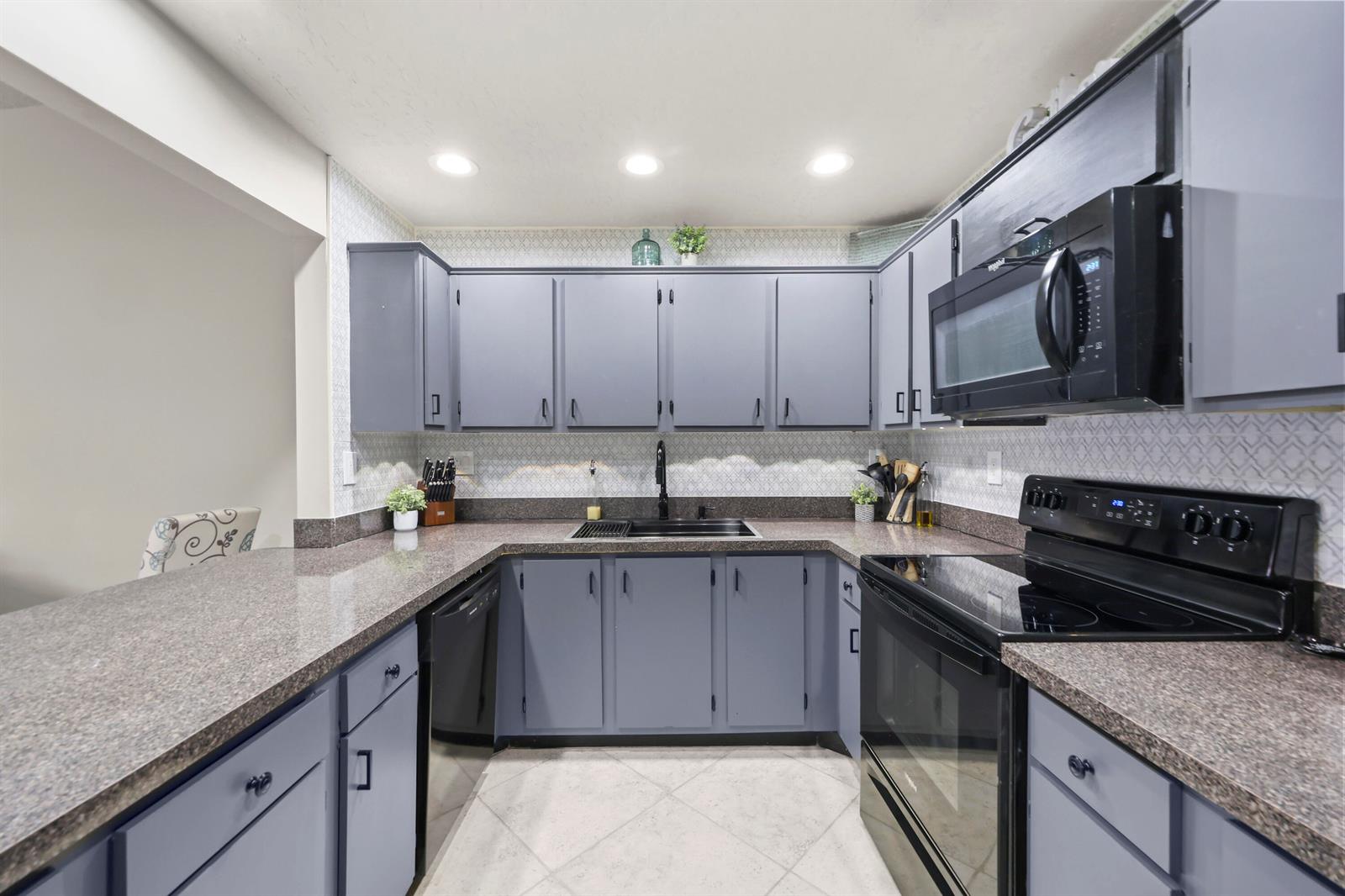 A kitchen features gray cabinets, dark granite countertops, black appliances, and a patterned tile backsplash — 39 Bethesda Park Circle # L39, Boynton Beach FL 33435, BOYNTON BEACH, FL