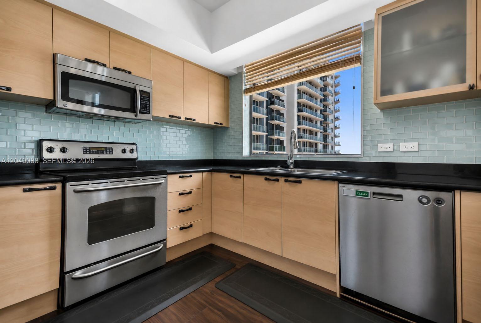 A kitchen features light wood cabinets, stainless steel appliances, black countertops, and a subway tile backsplash — 140 S Dixie Hwy # 501, Hollywood FL 33020, HOLLYWOOD, FL
