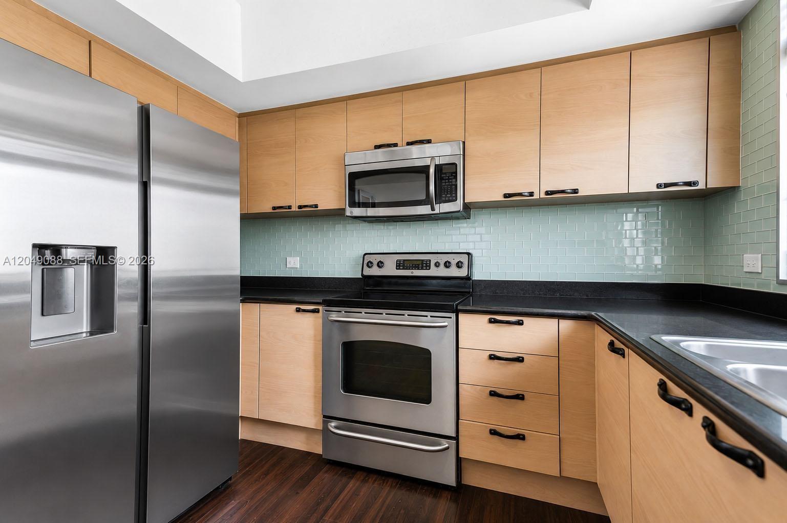 A kitchen features light wood cabinets, stainless steel appliances, black countertops, and a light green backsplash — 140 S Dixie Hwy # 501, Hollywood FL 33020, HOLLYWOOD, FL