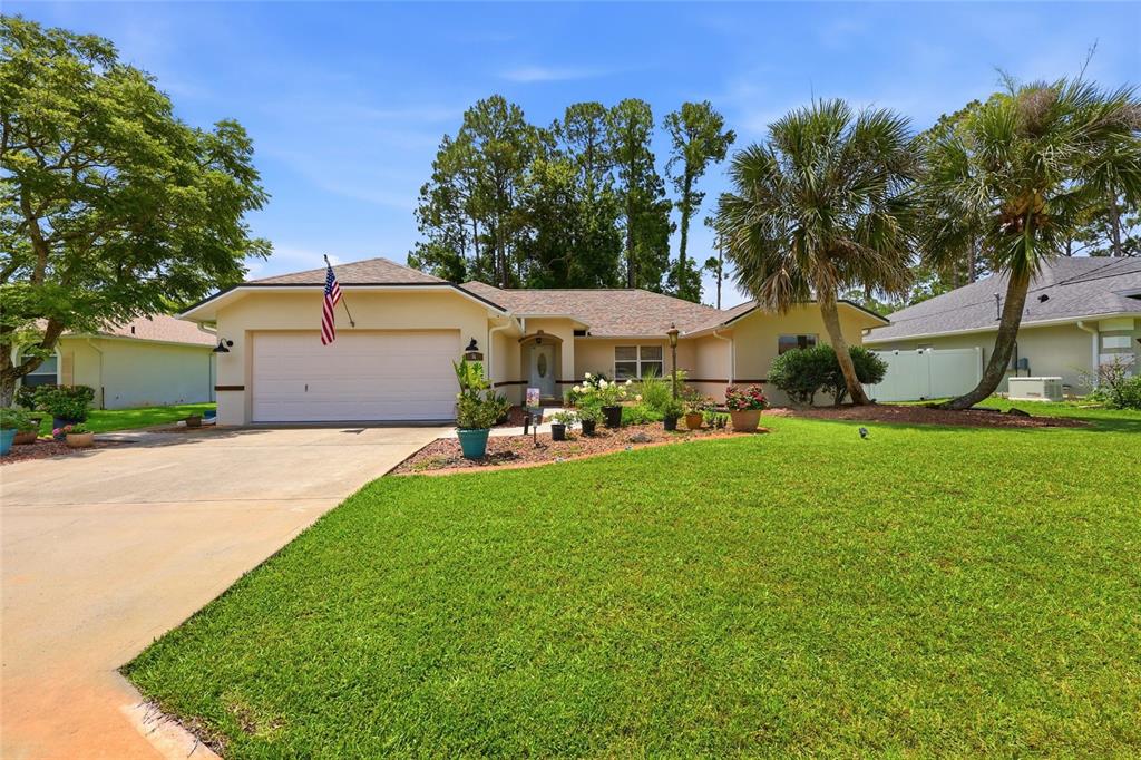 A single-story house with a two-car garage, a front lawn, and palm trees — 56 BASSETT LANE, PALM COAST, FL