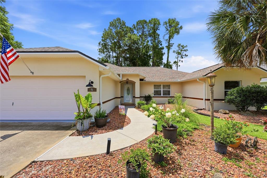 A single-story house with a beige exterior, a two-car garage, and a curved concrete walkway — 56 BASSETT LANE, PALM COAST, FL