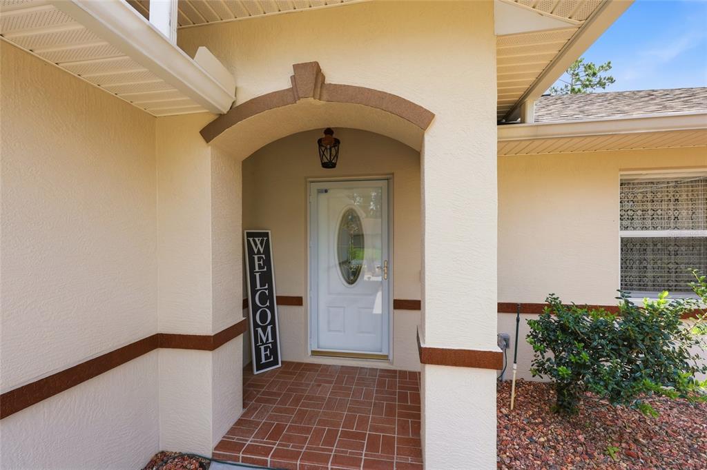 A covered entryway features a white front door, a welcome sign, and tiled flooring — 56 BASSETT LANE, PALM COAST, FL