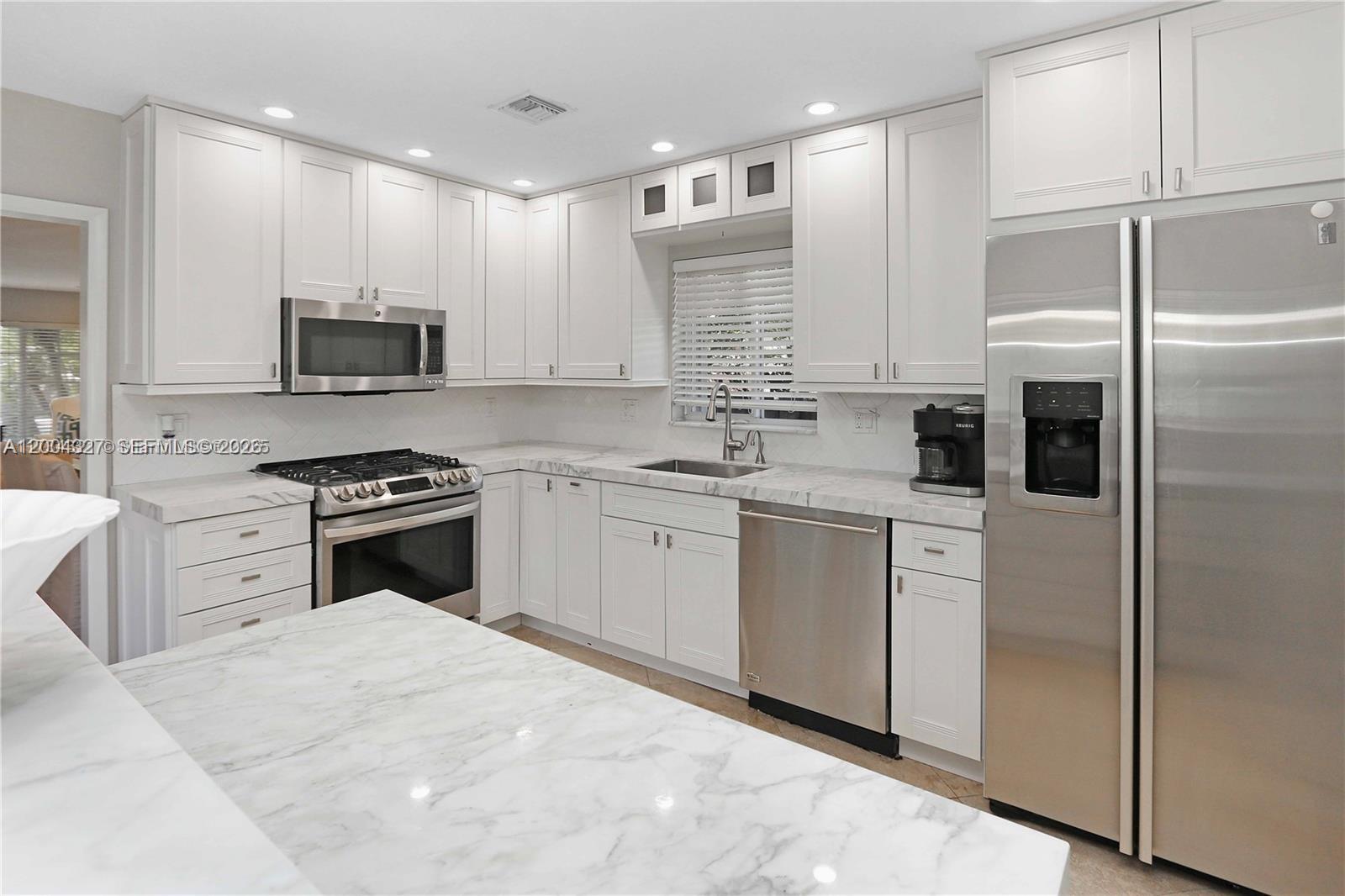 A kitchen features white cabinetry, stainless steel appliances, and a marble-patterned countertop island — 1147 Buchanan St, Hollywood FL 33019, HOLLYWOOD, FL