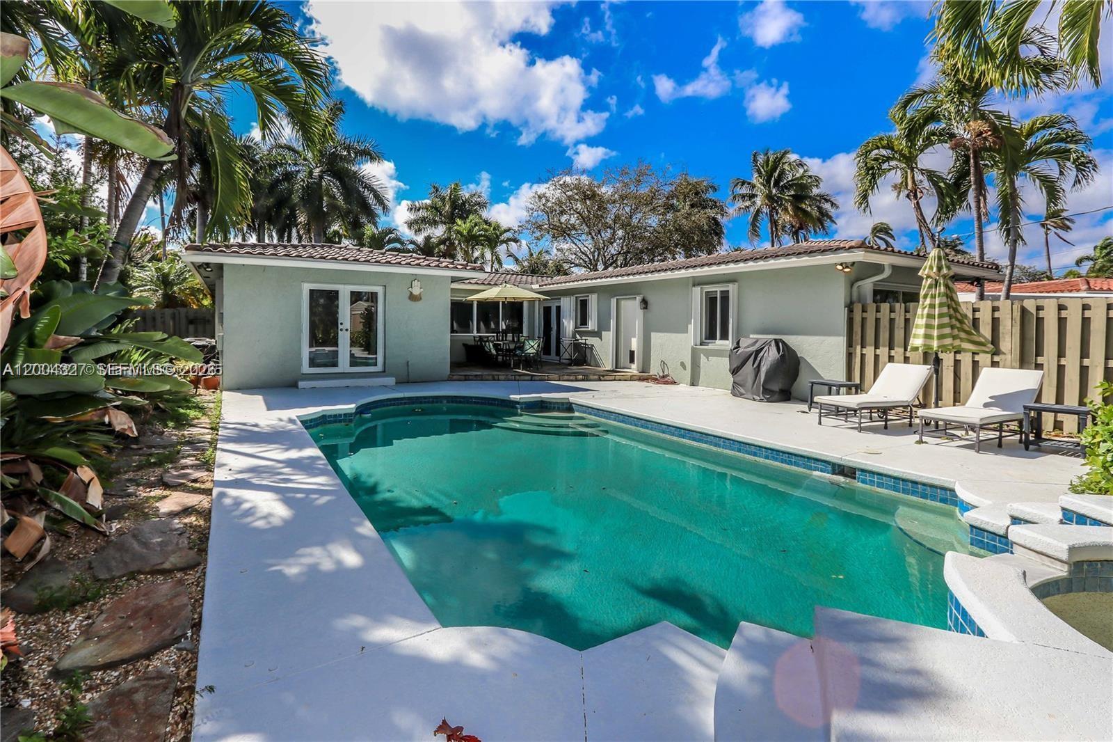 A backyard features a swimming pool, patio furniture, and palm trees against a blue sky — 1147 Buchanan St, Hollywood FL 33019, HOLLYWOOD, FL