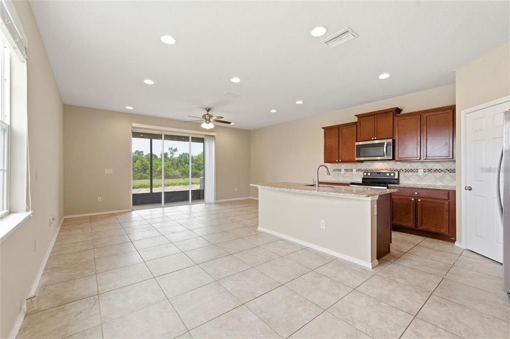 An open-concept kitchen and living area with tile flooring, granite countertops, and sliding glass doors — 8961 TURNSTONE HAVEN PLACE, TAMPA, FL