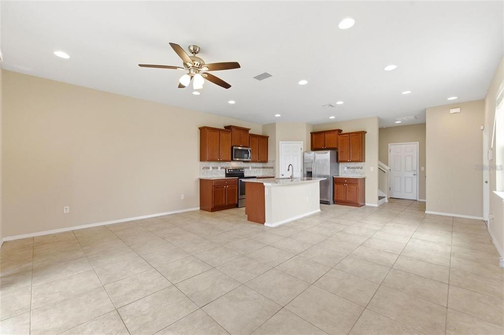 An open-concept kitchen features wood cabinets, stainless steel appliances, and tile flooring — 8961 TURNSTONE HAVEN PLACE, TAMPA, FL
