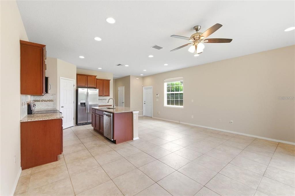 A kitchen with wood cabinets and a granite island opens into a large tiled room — 8961 TURNSTONE HAVEN PLACE, TAMPA, FL