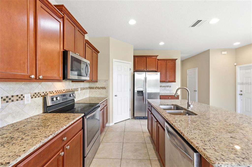 A kitchen features wood cabinets, granite countertops, stainless steel appliances, and a central island — 8961 TURNSTONE HAVEN PLACE, TAMPA, FL