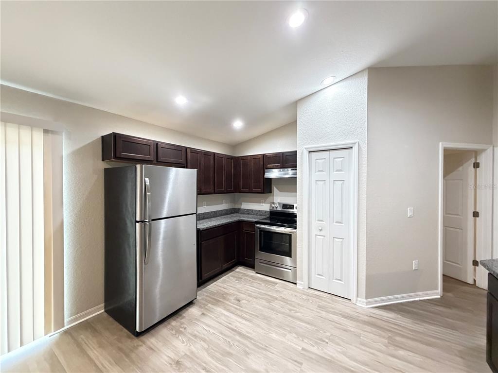 A kitchen features dark wood cabinets, stainless steel appliances, granite countertops, and light wood flooring — 2 BAHIA COURT RUN, OCALA, FL