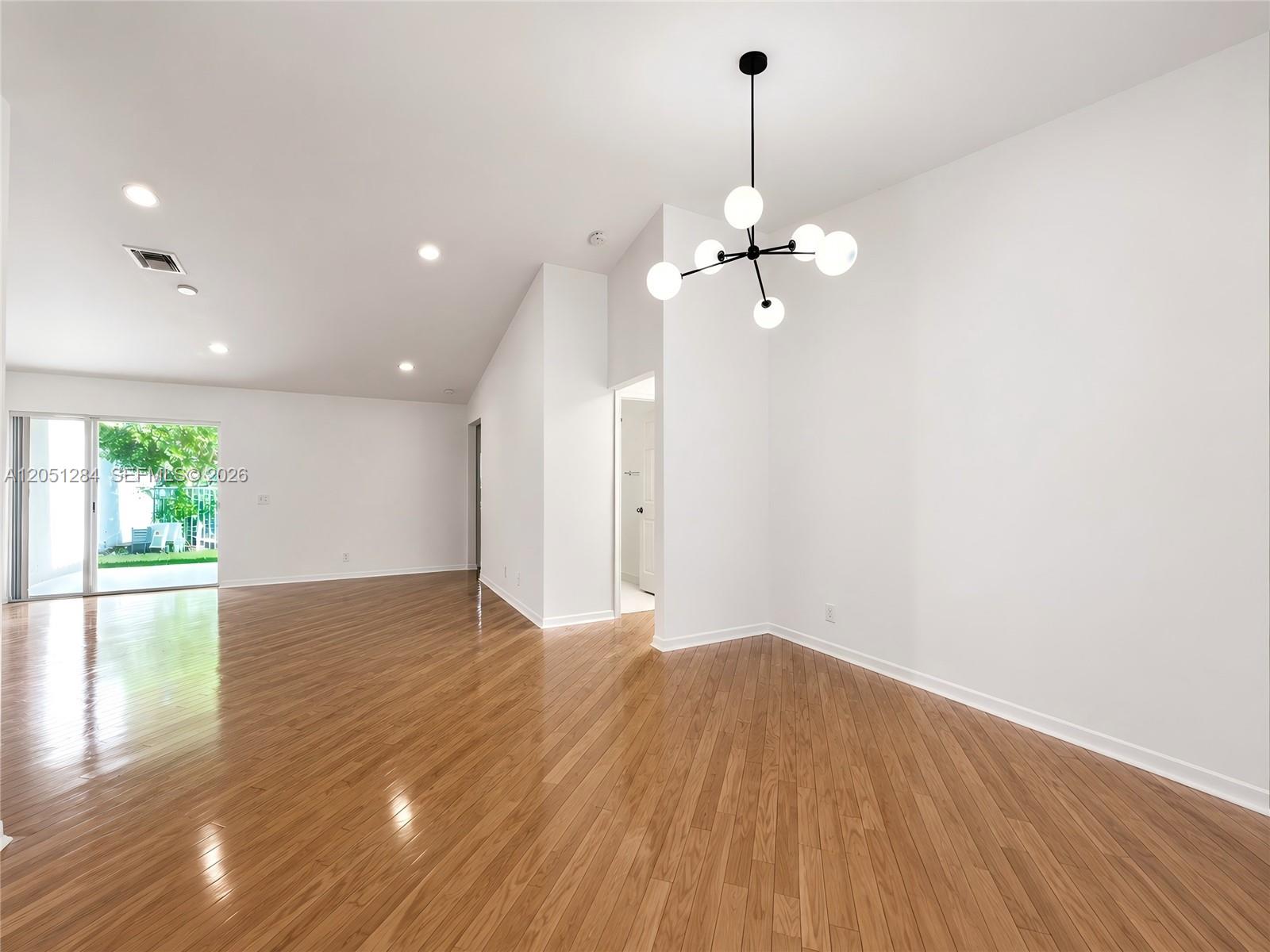 An empty room features hardwood floors, white walls, a modern chandelier, and a sliding glass door — 2082 Borealis Way, Weston FL 33327, WESTON, FL