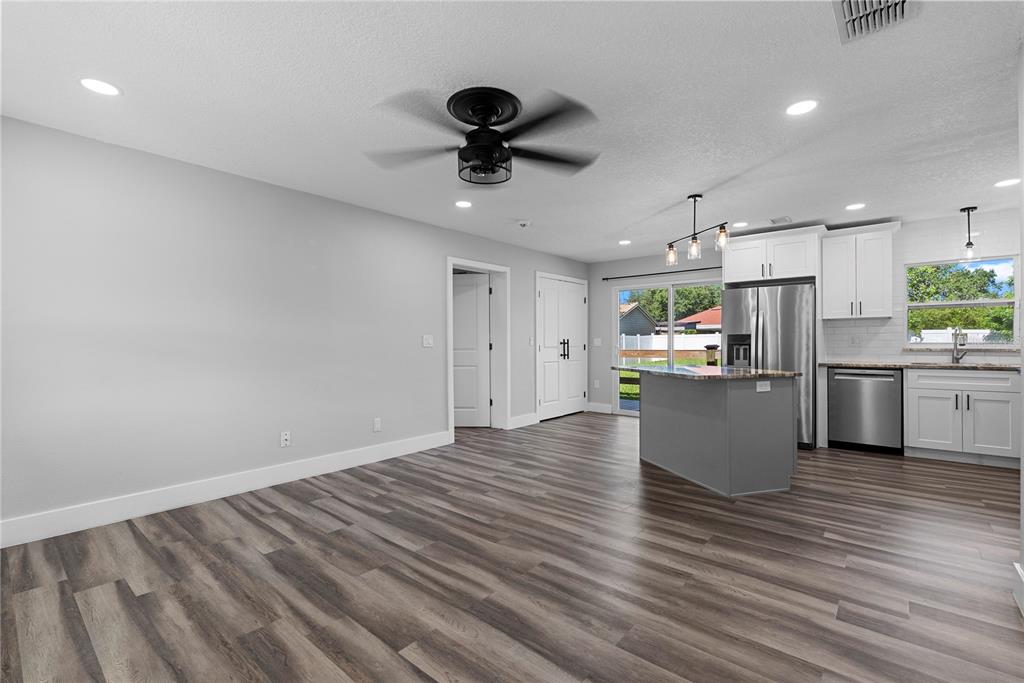 An open-concept kitchen and living area features gray wood-look flooring, white cabinets, and an island — 1350 SASOON AVENUE, ORLANDO, FL