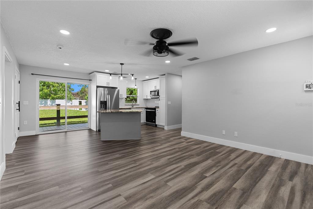 An open-concept kitchen and living area features wood-look flooring, white cabinets, and a sliding door — 1350 SASOON AVENUE, ORLANDO, FL