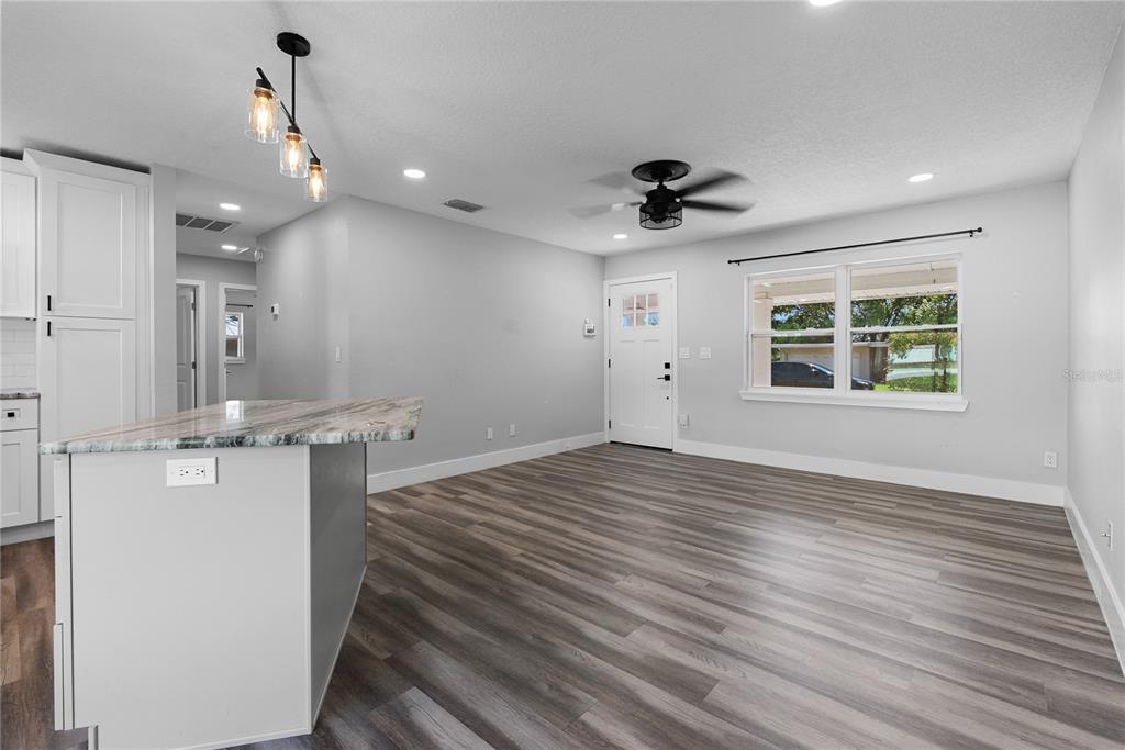 A kitchen island with granite countertops overlooks an open-concept living area with wood-look flooring — 1350 SASOON AVENUE, ORLANDO, FL