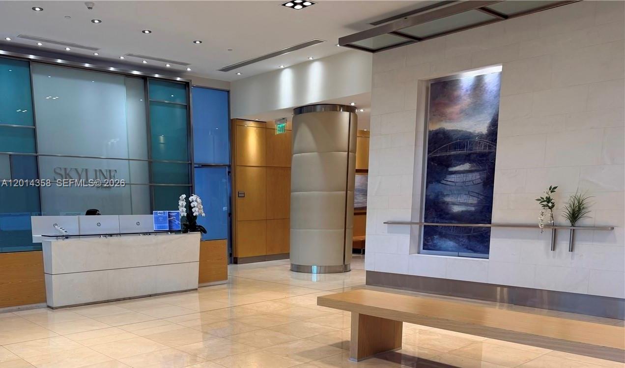 A modern building lobby features a reception desk, tiled floors, and a decorative wall mural — 2101 Brickell Ave # 1808, Miami FL 33129, MIAMI, FL