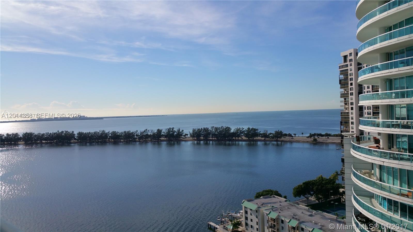 A high-angle view shows a calm bay with a tree-lined shore and a modern balcony — 2101 Brickell Ave # 1808, Miami FL 33129, MIAMI, FL