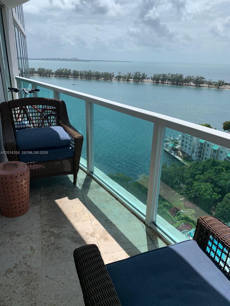 A balcony with wicker chairs overlooks a bay with a distant shoreline and trees — 2101 Brickell Ave # 1808, Miami FL 33129, MIAMI, FL