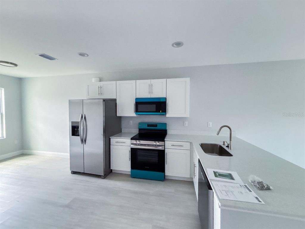 A kitchen features white cabinets, stainless steel appliances, a teal stove, and a peninsula countertop — 11 TROUT WAY UNIT A, POINCIANA, FL