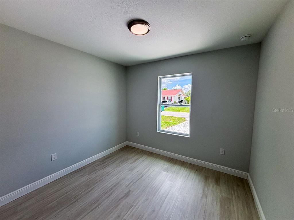 An empty room features light gray walls, wood-look flooring, a single window, and a ceiling light — 11 TROUT WAY UNIT A, POINCIANA, FL