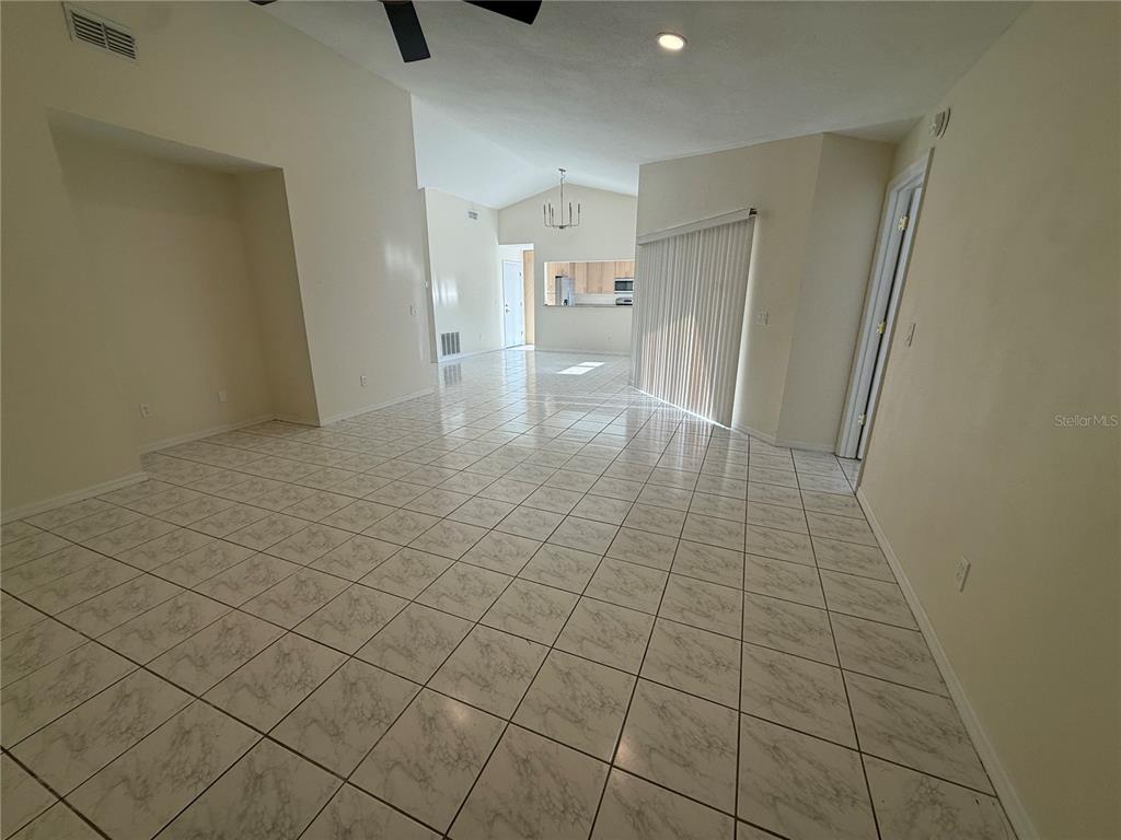 A bright, open-concept living area features light-colored tile flooring, vaulted ceilings, and a sliding glass door — 8102 S IBIZA COURT, ORLANDO, FL