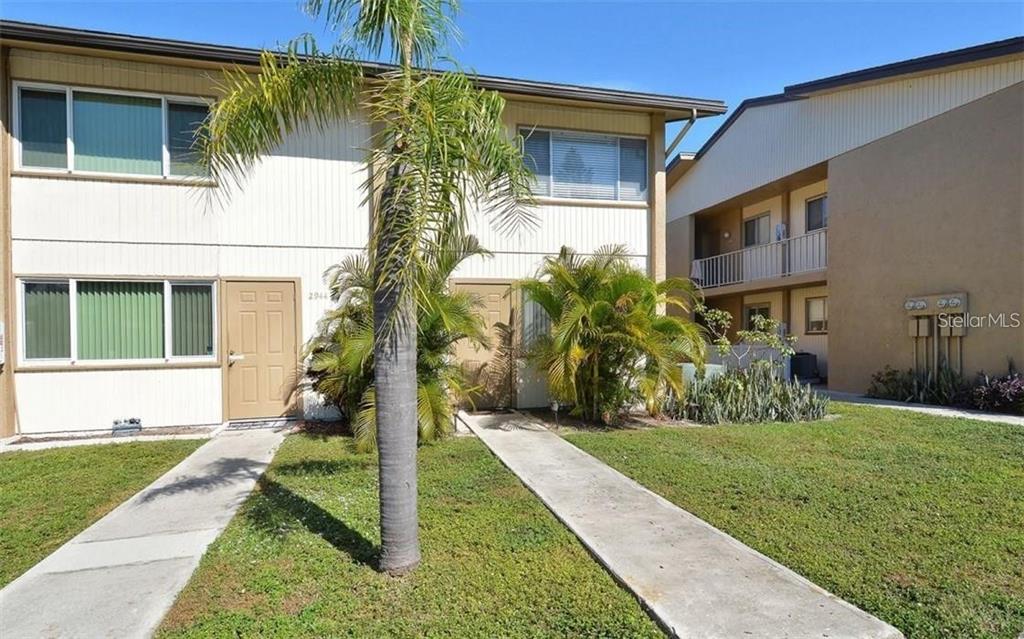 A two-story apartment building exterior features tan doors, white siding, and concrete walkways — 2946 CLARK ROAD UNIT 2946, SARASOTA, FL