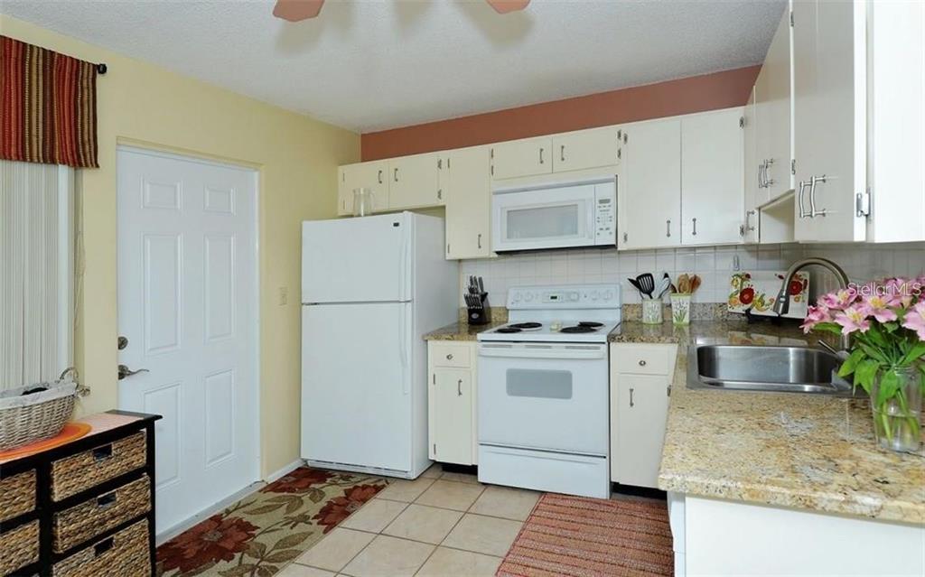 A kitchen features white appliances, light-colored cabinets, granite countertops, and a tiled floor — 2946 CLARK ROAD UNIT 2946, SARASOTA, FL