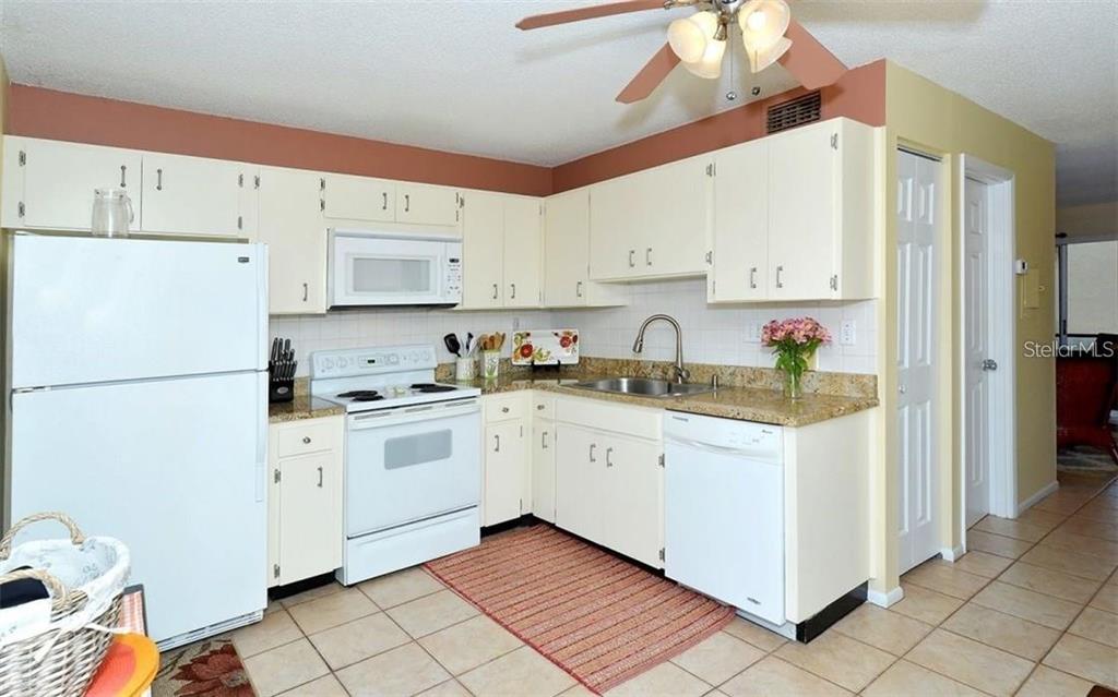 A kitchen with white cabinets, white appliances, granite countertops, and a tile floor — 2946 CLARK ROAD UNIT 2946, SARASOTA, FL