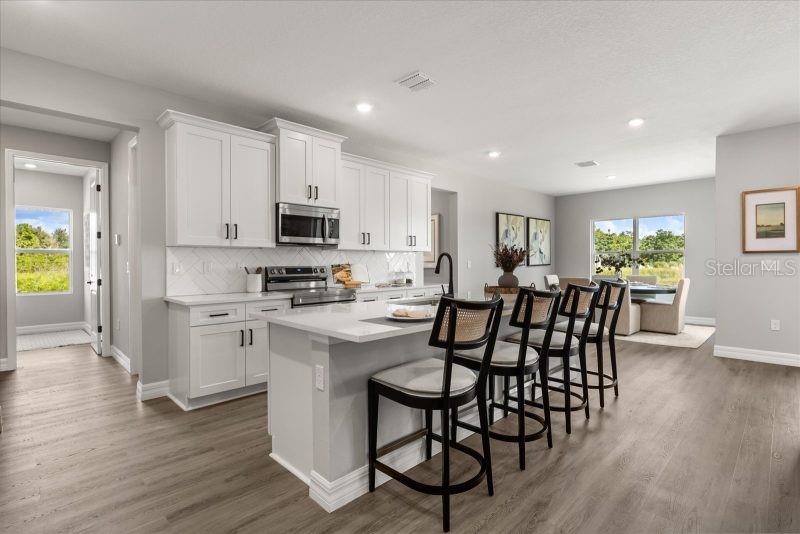 A modern kitchen features white cabinets, a central island with bar stools, and wood flooring — 2665 SW 162 LANE, OCALA, FL