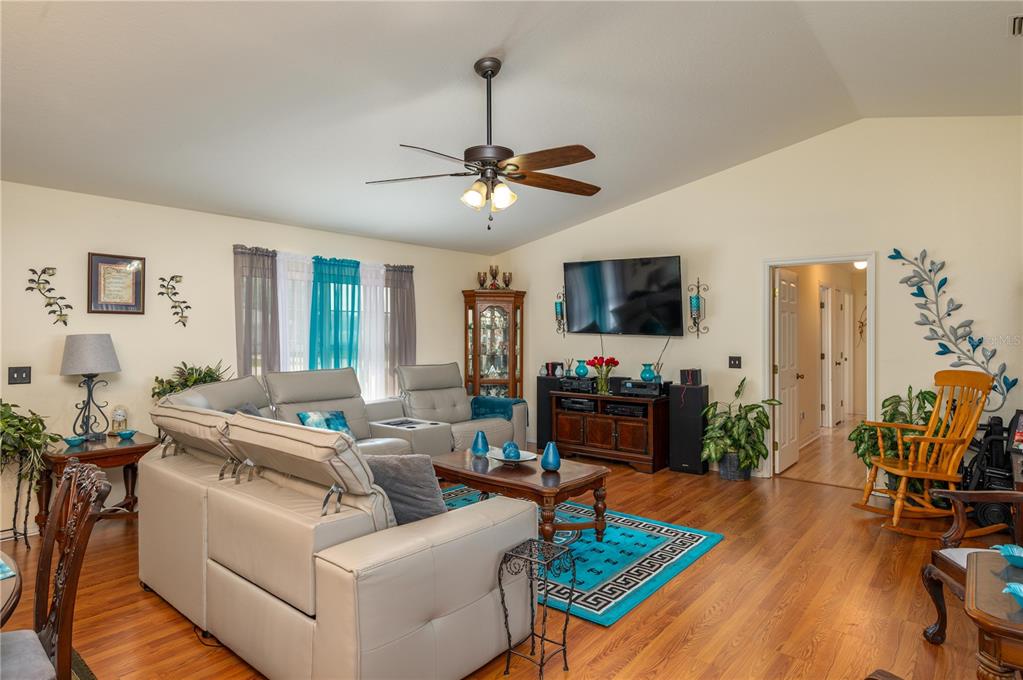 A living room features light-colored leather sofas, hardwood floors, a ceiling fan, and a television — 411 COUNTRY PINE ROAD, HAINES CITY, FL