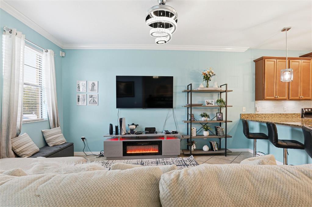 A living room with light blue walls, a wall-mounted TV, fireplace console, and open kitchen — 4390 FENNWOOD COURT, WESLEY CHAPEL, FL