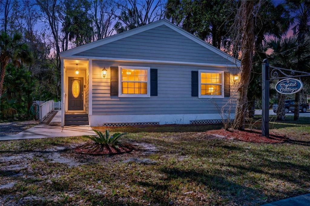 A gray cottage with a front porch, two windows with shutters, and a hanging sign — 110 NE CRYSTAL STREET, CRYSTAL RIVER, FL