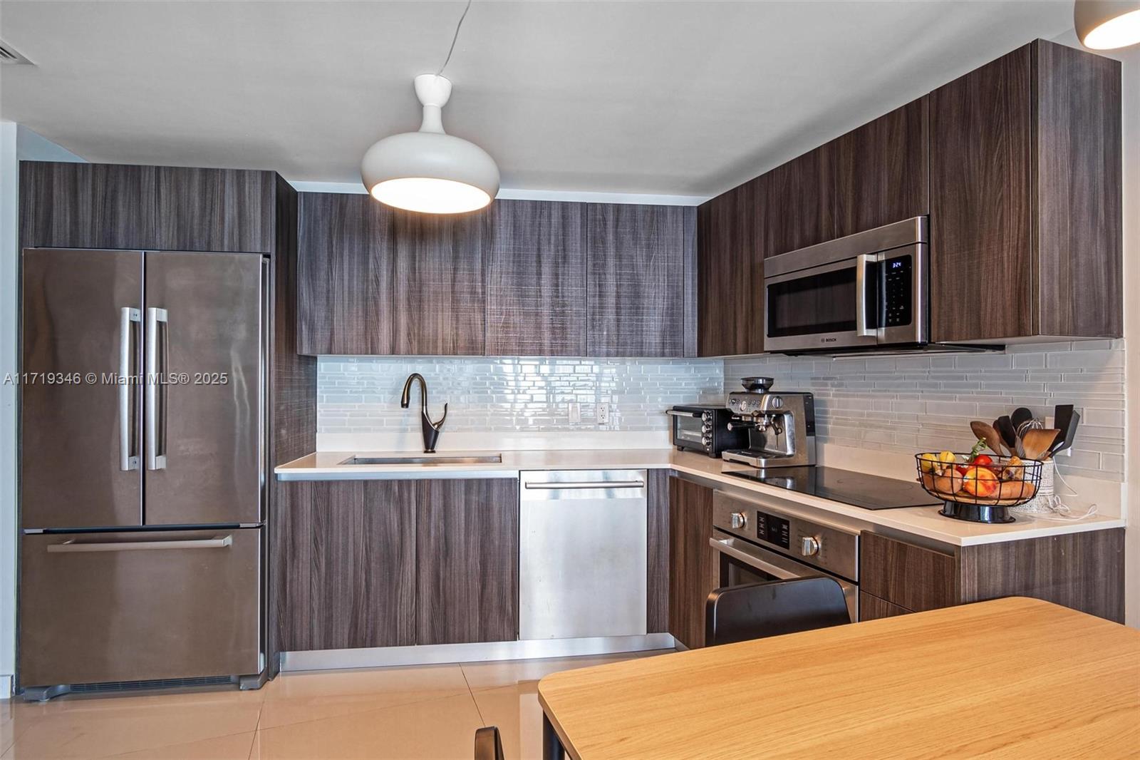 A kitchen features dark wood cabinets, stainless steel appliances, and a white subway tile backsplash — 488 NE 18th St # 401, Miami FL 33132, MIAMI, FL