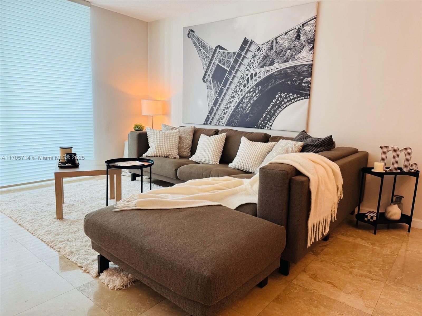 A living room features a brown sectional sofa, a large Eiffel Tower print, and tile flooring — 1200 Brickell Bay Dr # 3220, Miami FL 33131, MIAMI, FL