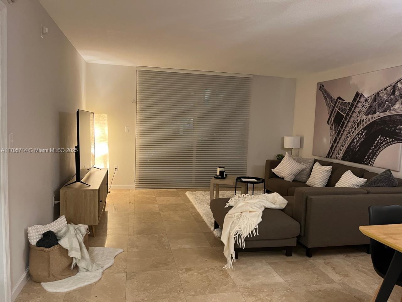 A living room features a grey sectional sofa, a television on a console, and tile flooring — 1200 Brickell Bay Dr # 3220, Miami FL 33131, MIAMI, FL