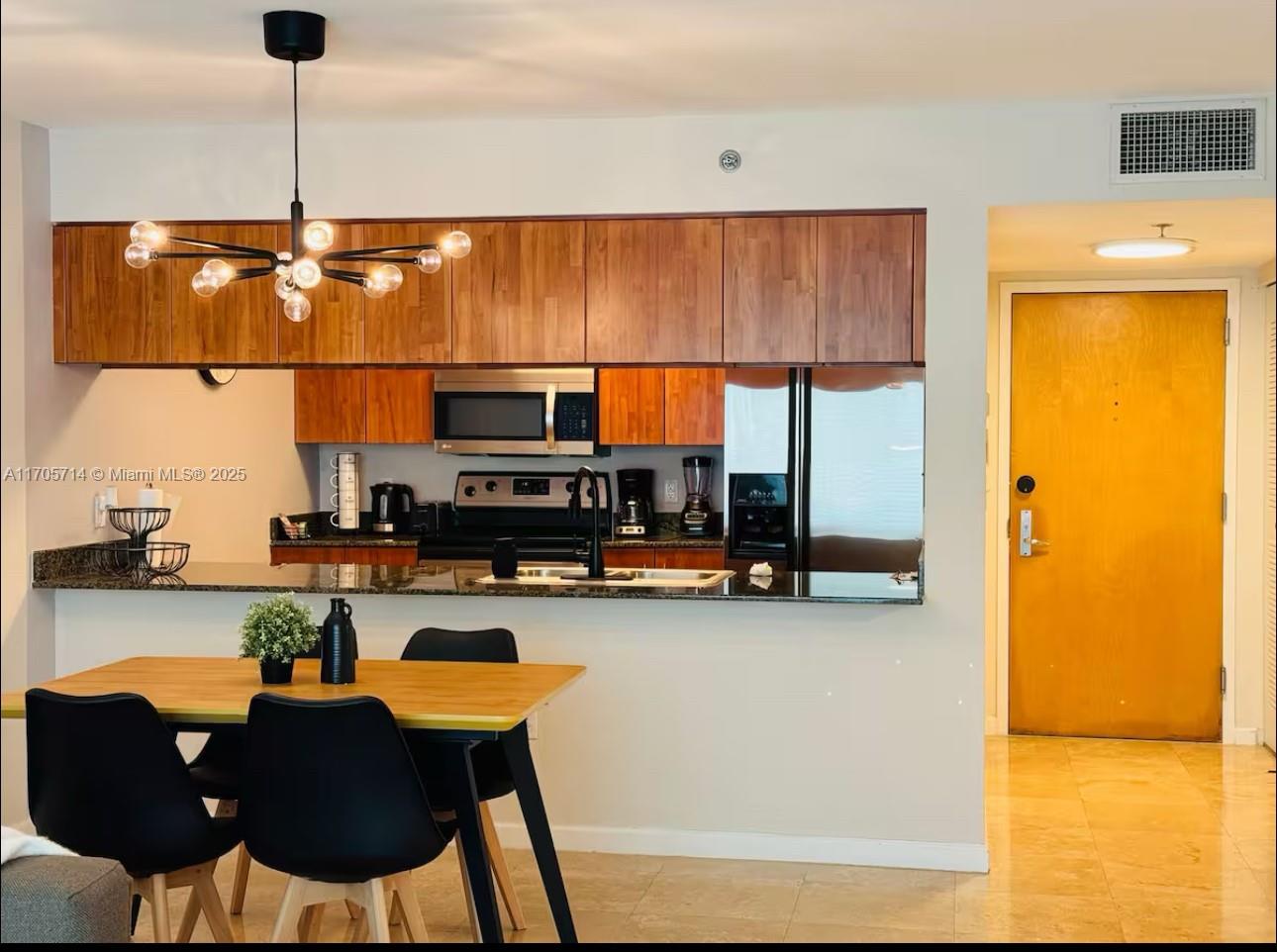 A kitchen with wood cabinets and a breakfast bar overlooks a dining area with chairs — 1200 Brickell Bay Dr # 3220, Miami FL 33131, MIAMI, FL