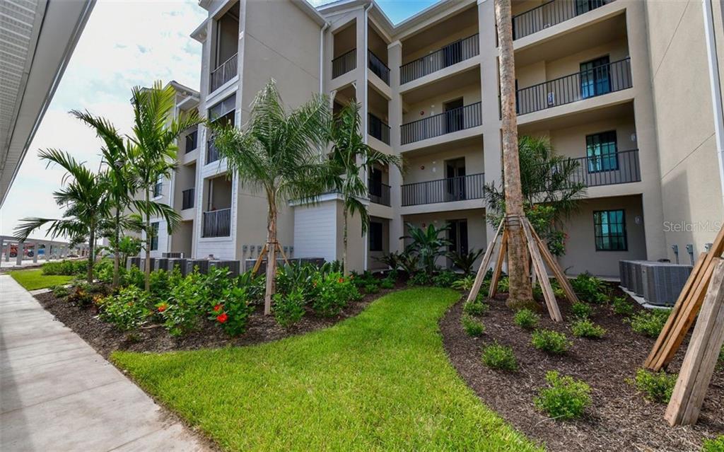 A multi-story apartment building exterior features balconies, palm trees, and a landscaped lawn — 17520 GAWTHROP DRIVE UNIT 203, LAKEWOOD RANCH, FL
