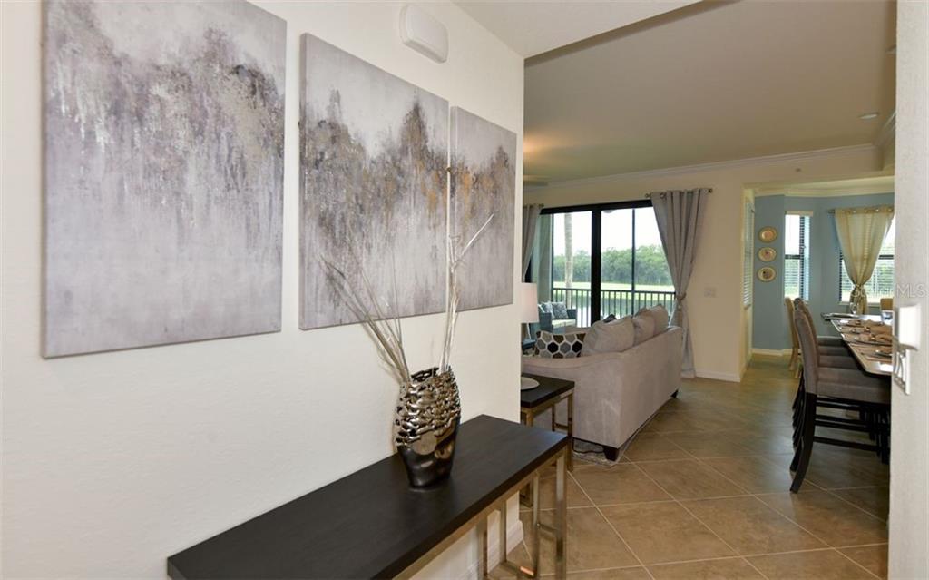 A hallway with a console table and wall art leads into a living and dining area — 17520 GAWTHROP DRIVE UNIT 203, LAKEWOOD RANCH, FL