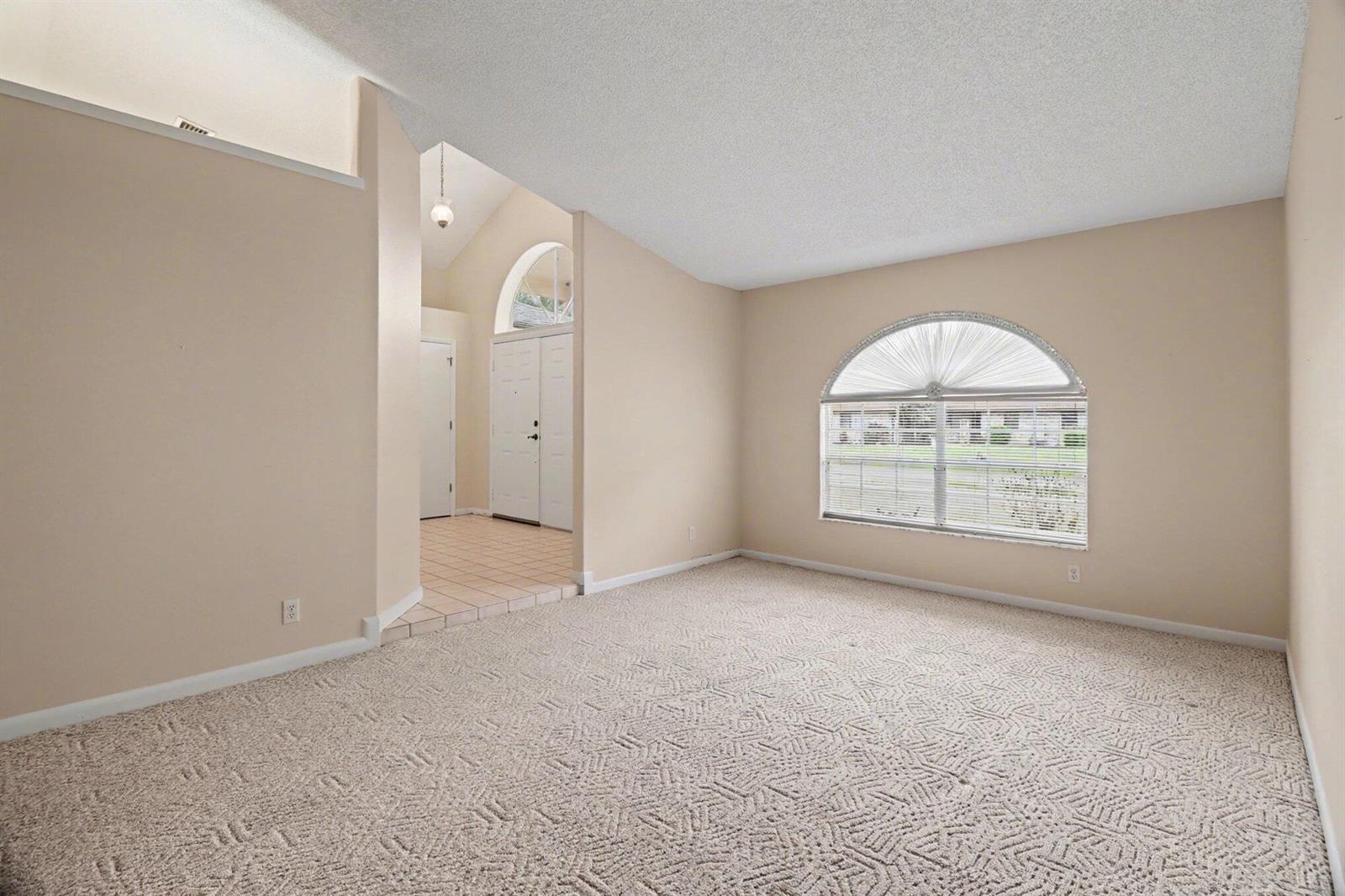 A carpeted living room with a vaulted ceiling and an arched window overlooks the entryway — 875 Gabriel Avenue NE, Palm Bay FL 32907, PALM BAY, FL
