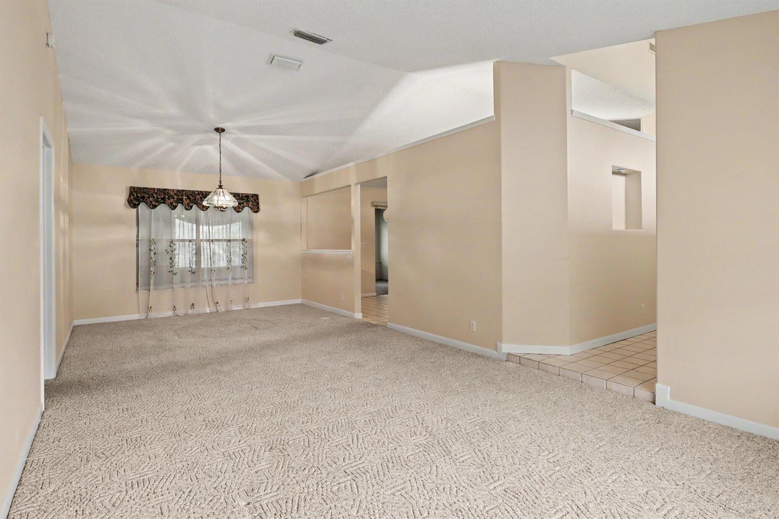 A carpeted living room features a vaulted ceiling, a chandelier, and a tiled entryway — 875 Gabriel Avenue NE, Palm Bay FL 32907, PALM BAY, FL