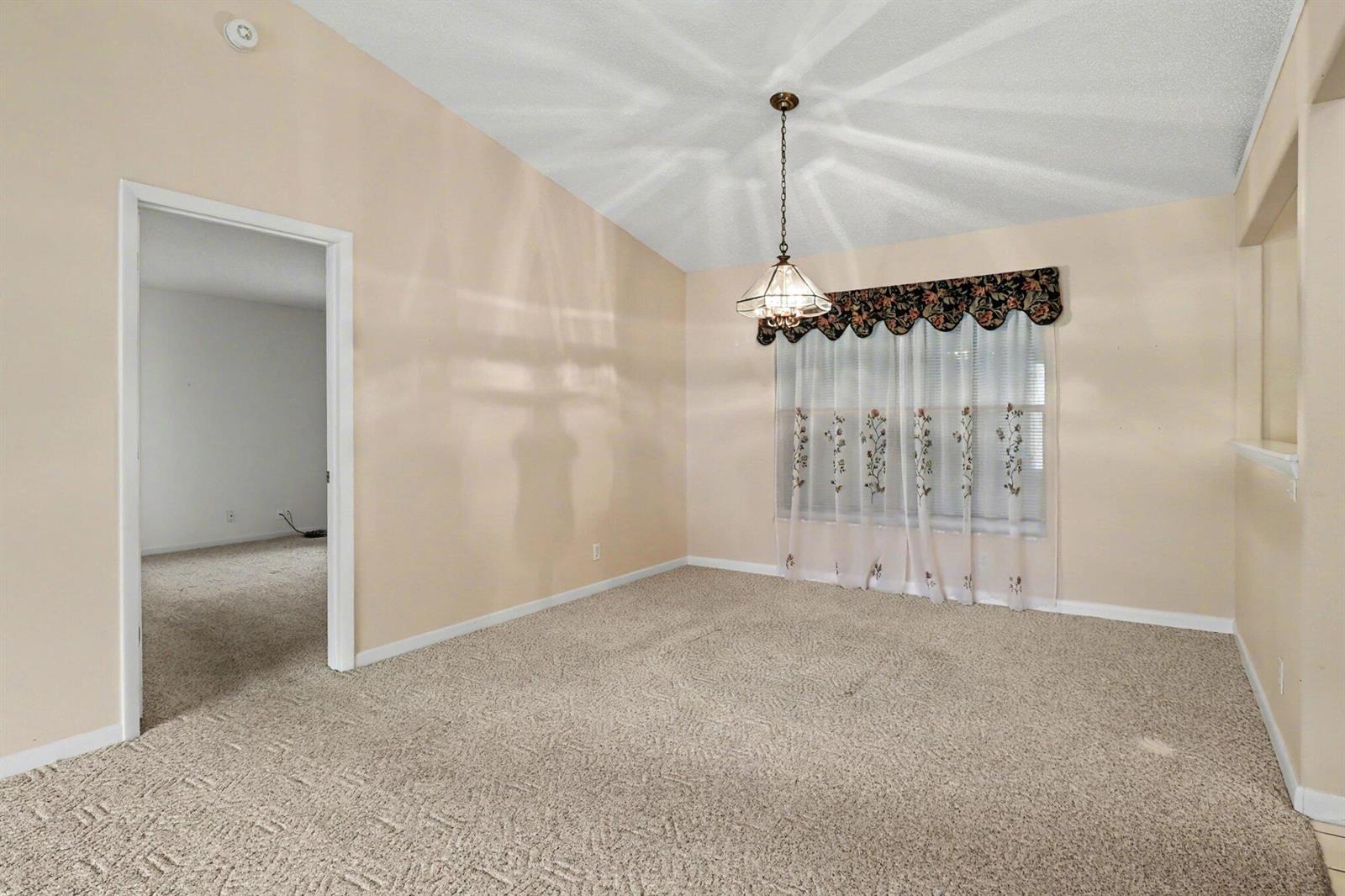 A carpeted dining room features a vaulted ceiling, a hanging light fixture, and window curtains — 875 Gabriel Avenue NE, Palm Bay FL 32907, PALM BAY, FL
