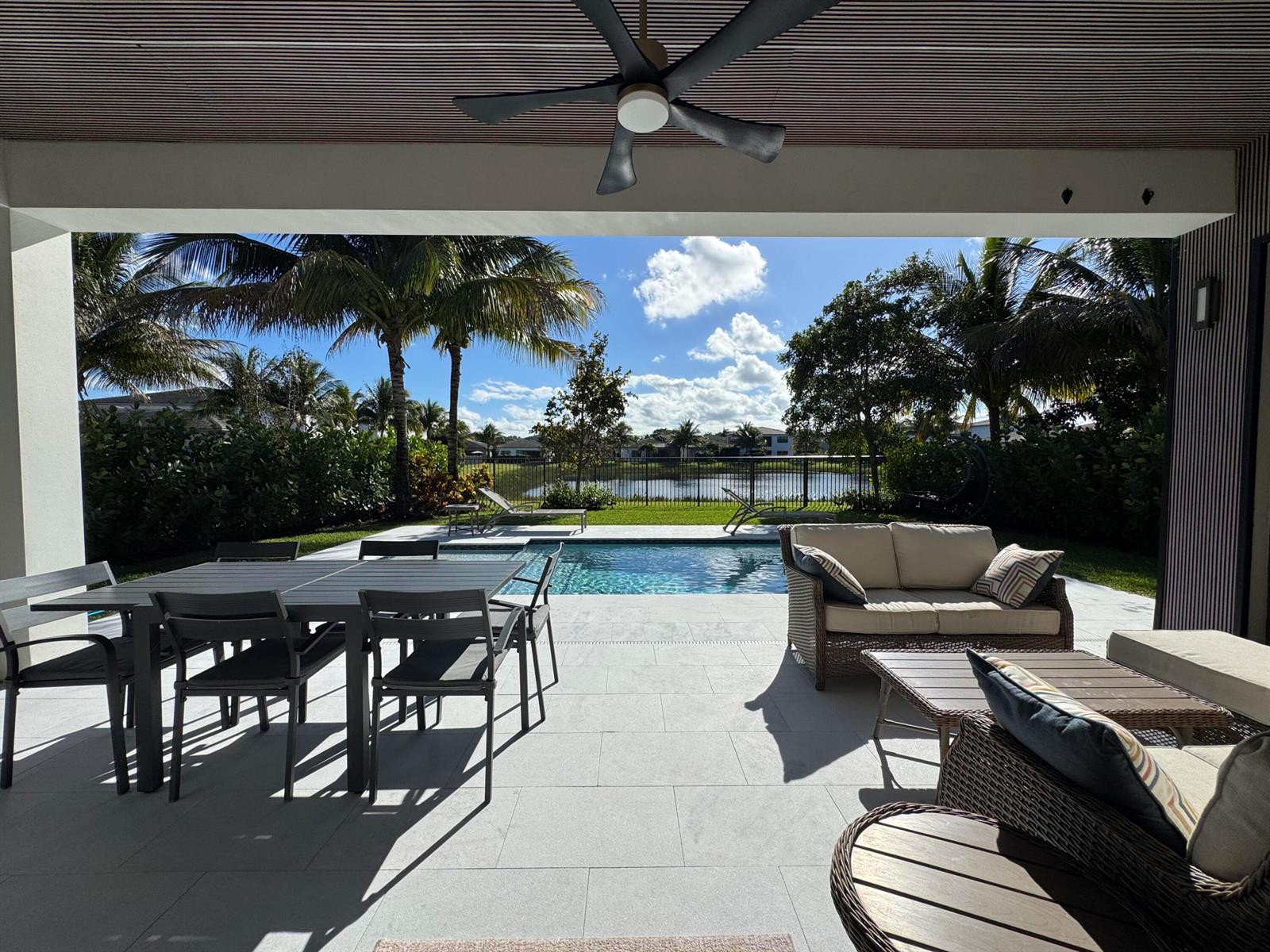 A covered patio features a dining set and lounge furniture overlooking a pool and lake — 8606 Tower Bridge Court, Boca Raton FL 33496, BOCA RATON, FL