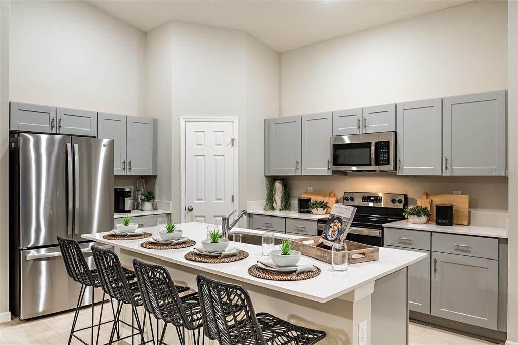 A kitchen features gray cabinets, stainless steel appliances, a white island, and black woven stools — 5828 HEAVEN ROAD, HAINES CITY, FL